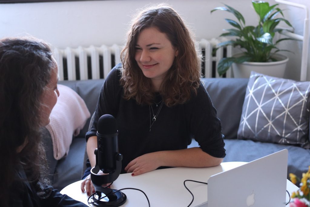 Two women recording a podcast at a table. Podcasts can help you improve your English listening skills.