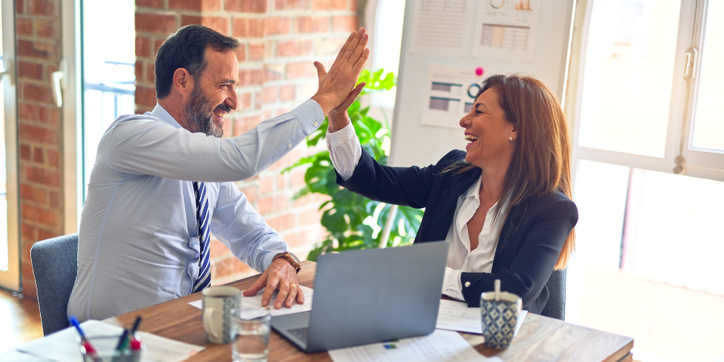 Two people at a conference table congratulate each other after going above and beyond.