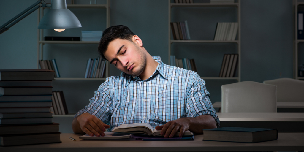 A student falling asleep while studying with his books.