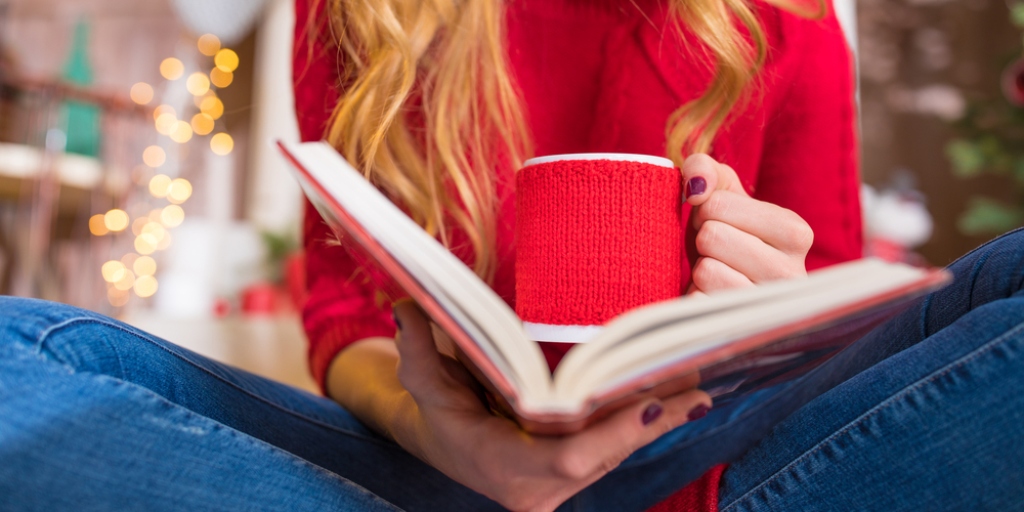A young woman reading a book and holding a mug of a hot drink