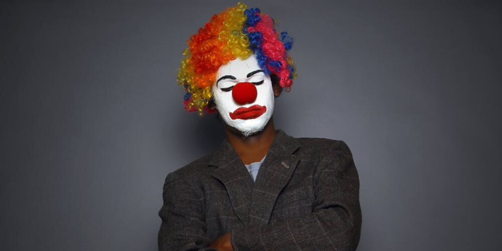 A man wearing a suit coat and a clown face expresses disappointment