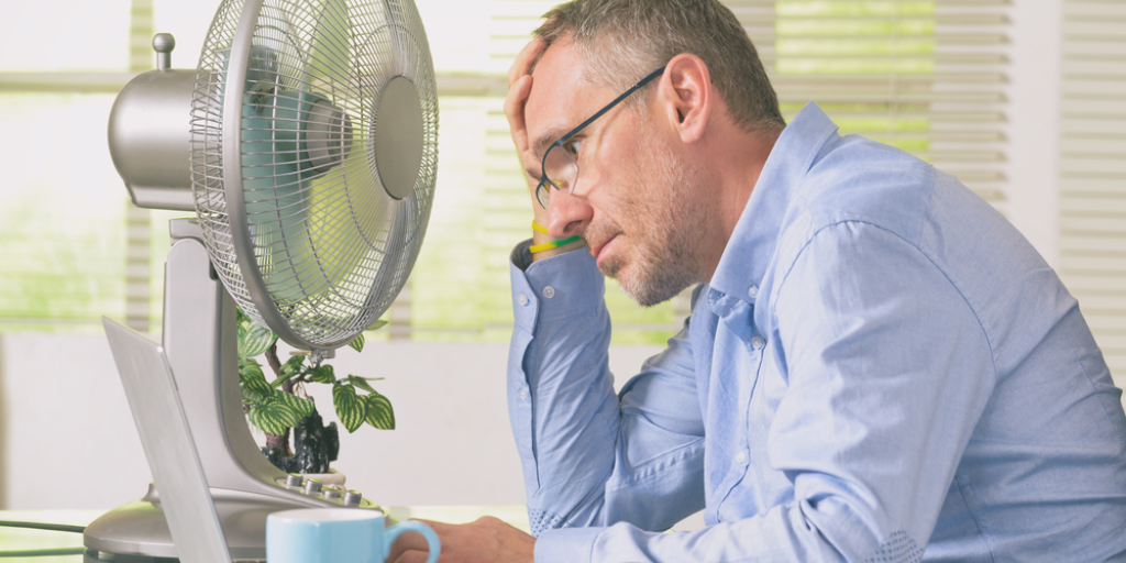 A man sitting at a desk in front of a fan.