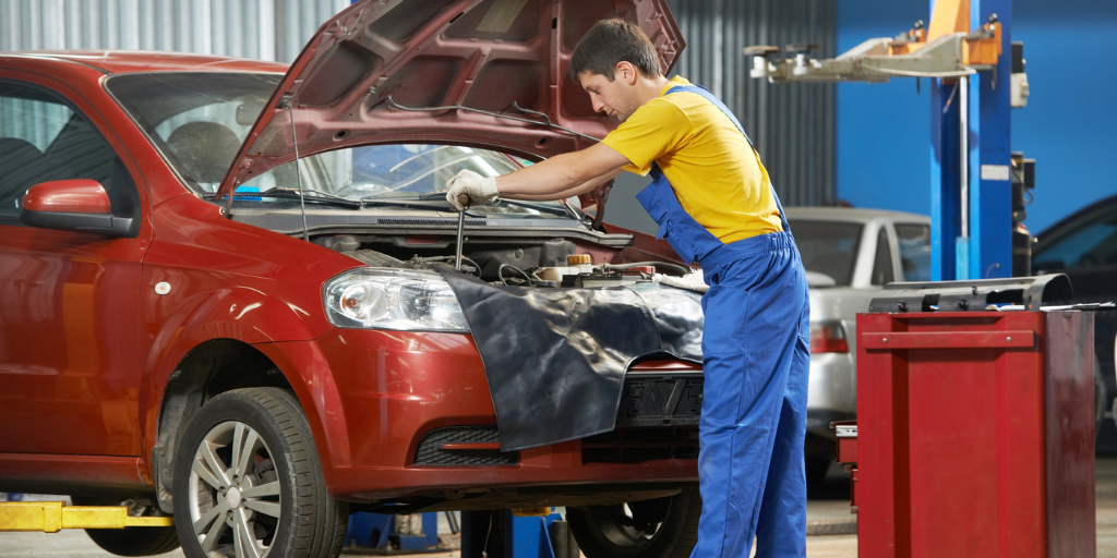 An auto mechanic performing repairs on a red car