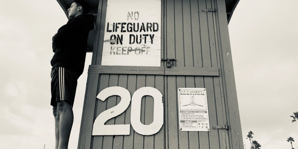 A man wearing shorts and a sweatshirt stands by the lifeguard stand at a beach