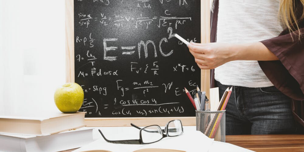 A student with a chalkboard showing equations in the background