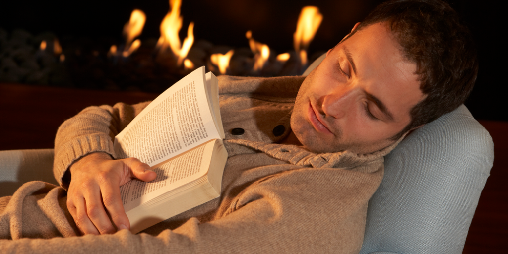 A man sleeping with a book in his hand and the light on