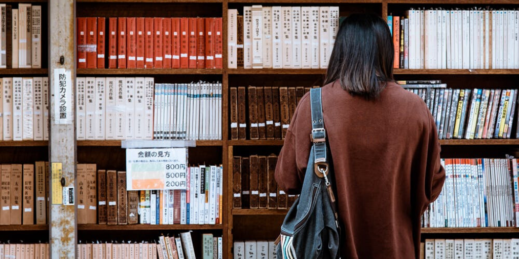 A woman browses books on the shelves of a bookstore or library
