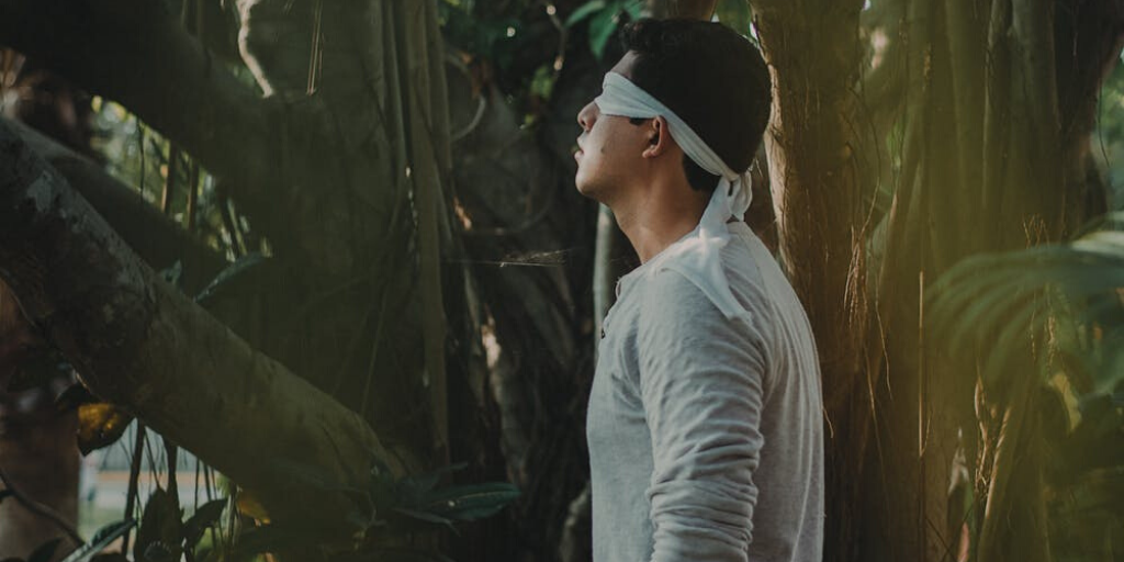 A man is blindfolded in the forest