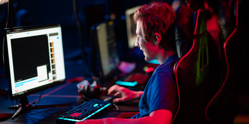 A man in a gamer chair in a dark room plays a video game.