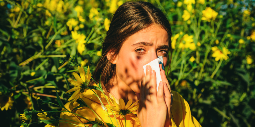 A girl suffers from pollen allergy in front of a large stand of flowers