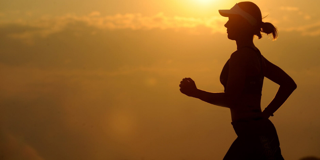 A woman wearing a visor goes for a run at sunset