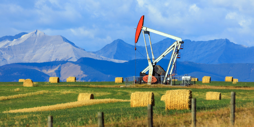 View of an oil rig in a prairie with mountains in the background