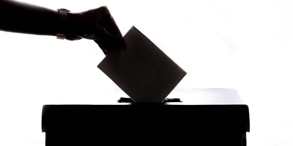 A person places a paper ballot into a wooden box