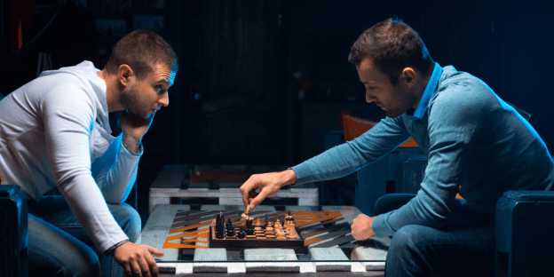 Two people hover over a chess board in an intense game.