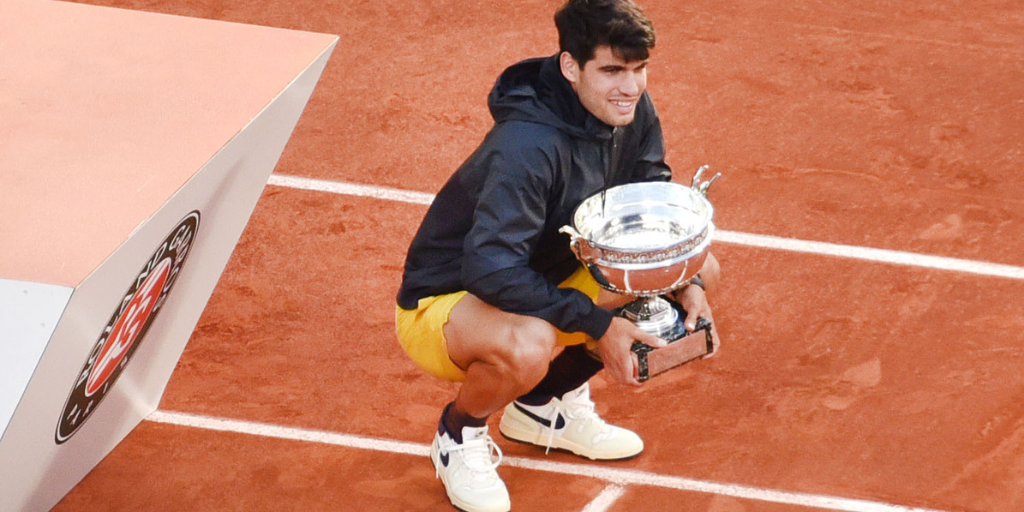 Carlos Alcaraz holding a trophy on the famous red clay courts, after winning the French Open in 2024