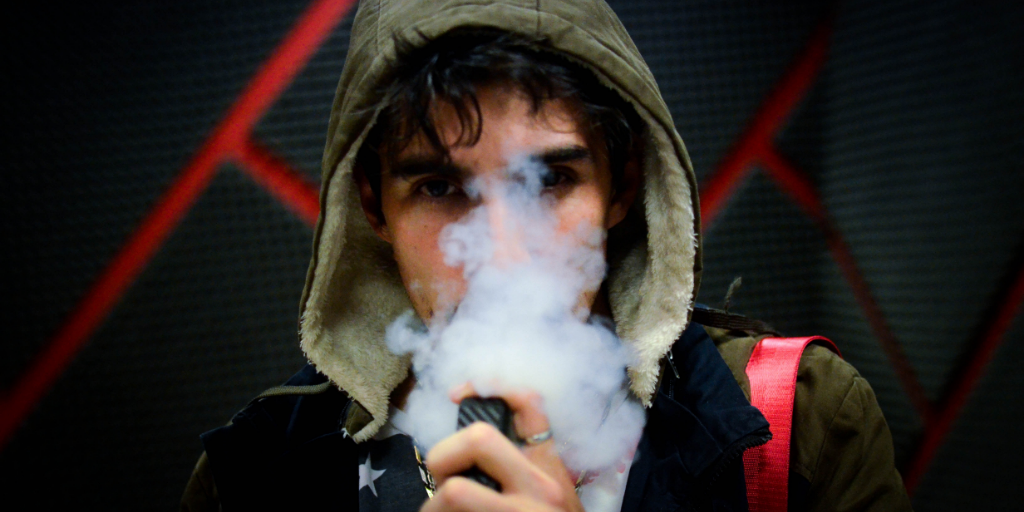 A man wearing a hoodie sweatshirt exhales a cloud of vapor