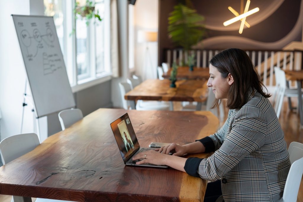 A woman at a table on a video call. Speaking English fluently takes time, but frequent practice helps.