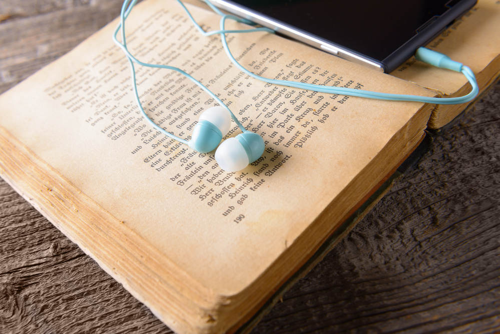 Headphones and mobile phone on an old book. Listening and reading at the same time can help you improve your language skills.