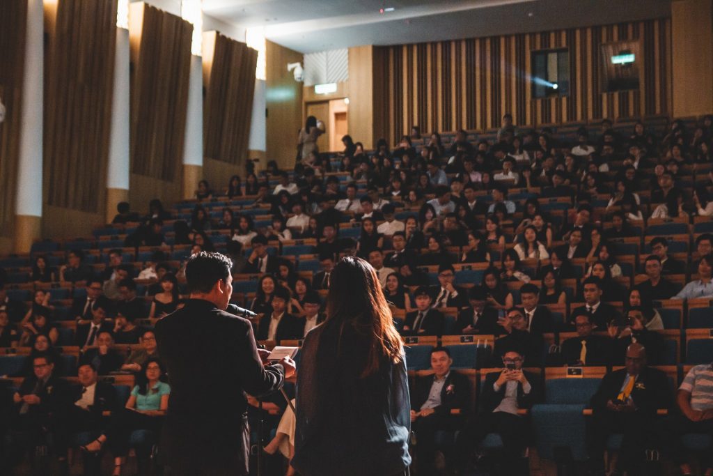 Two people address a large audience in a lecture hall.