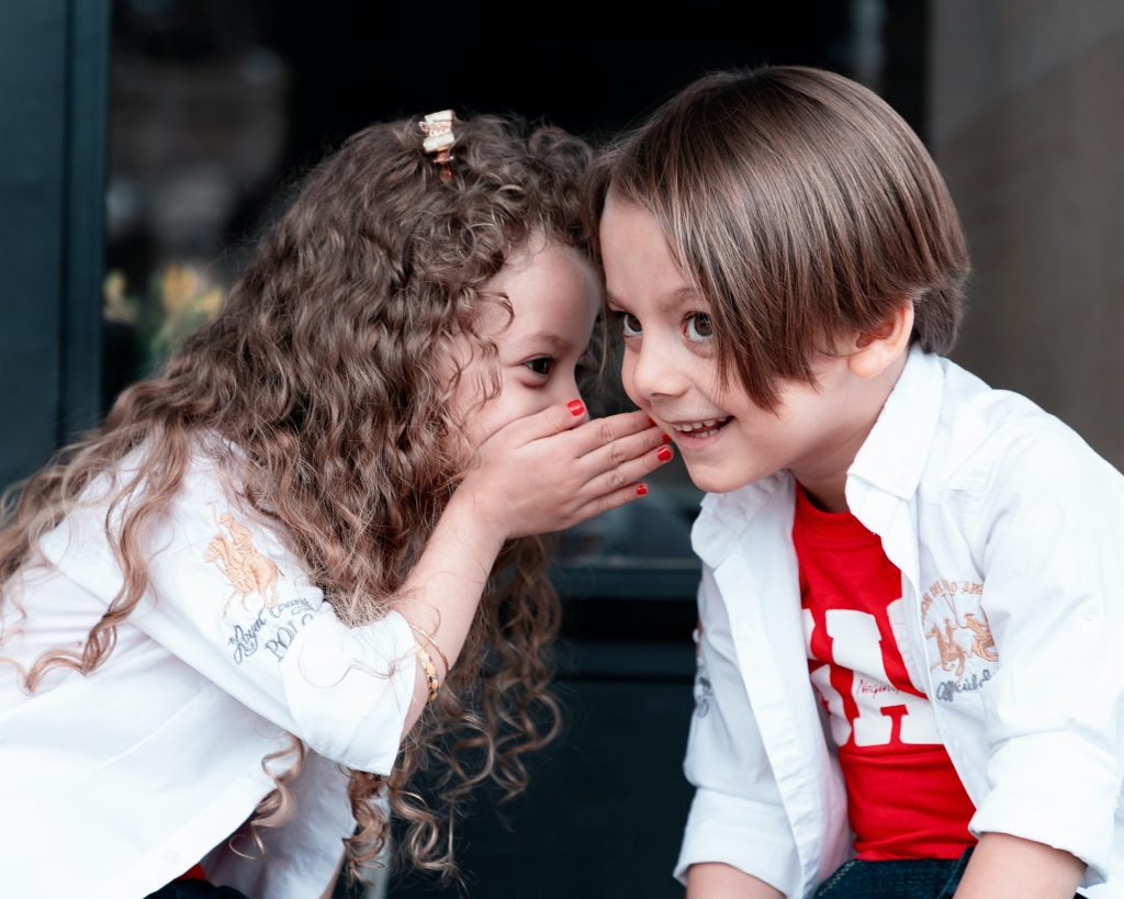 Two children whispering to each other. The children's game of "telephone" is fun in school, but not as fun when you're trying to be understood in the real world.